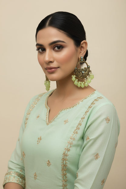 Naanu antique gold chandbali earrings with turquoise stones and lime green jade drops, featuring intricate peacock and floral engraving.
