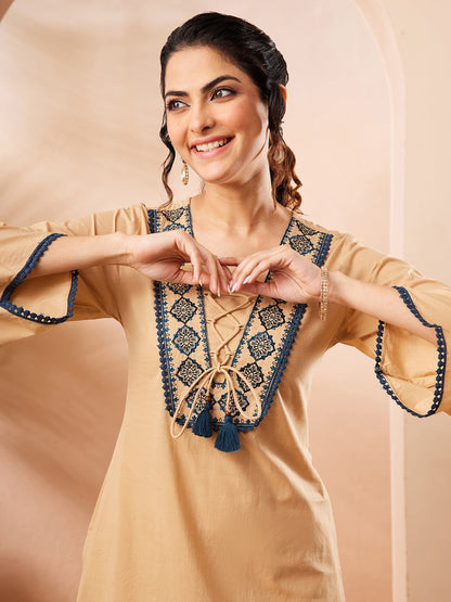 Naanu beige cotton top with embroidered V-neck and tassel tie, paired with navy Ajrakh print palazzo pants.