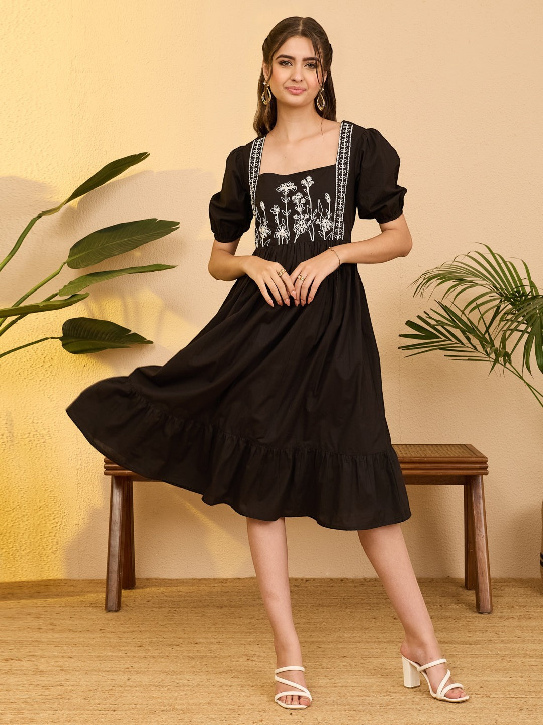 Naanu black cotton midi dress with white floral embroidery on bodice, square neckline, puff sleeves, and tiered ruffle hem.