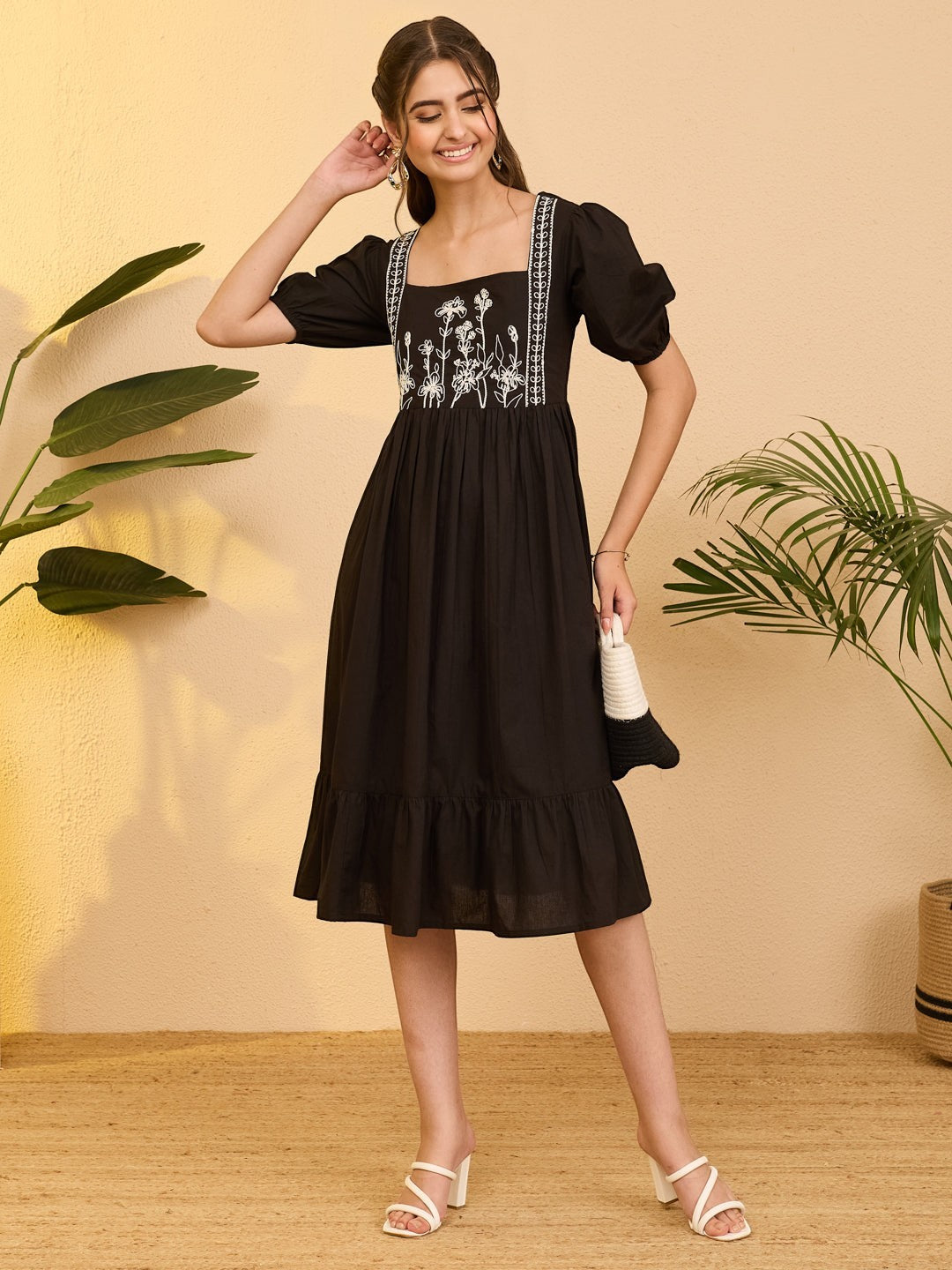 Naanu black cotton midi dress with white floral embroidery on bodice, square neckline, puff sleeves, and tiered hem.