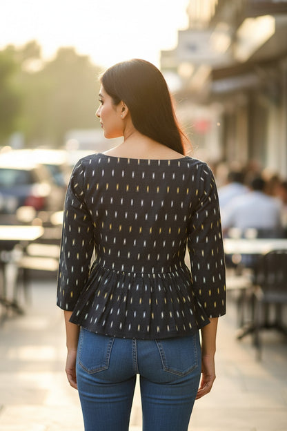 Naanu black ikat weave peplum top with white, yellow, and blue dash motifs, boat neck, 3/4 sleeves, and gathered peplum.