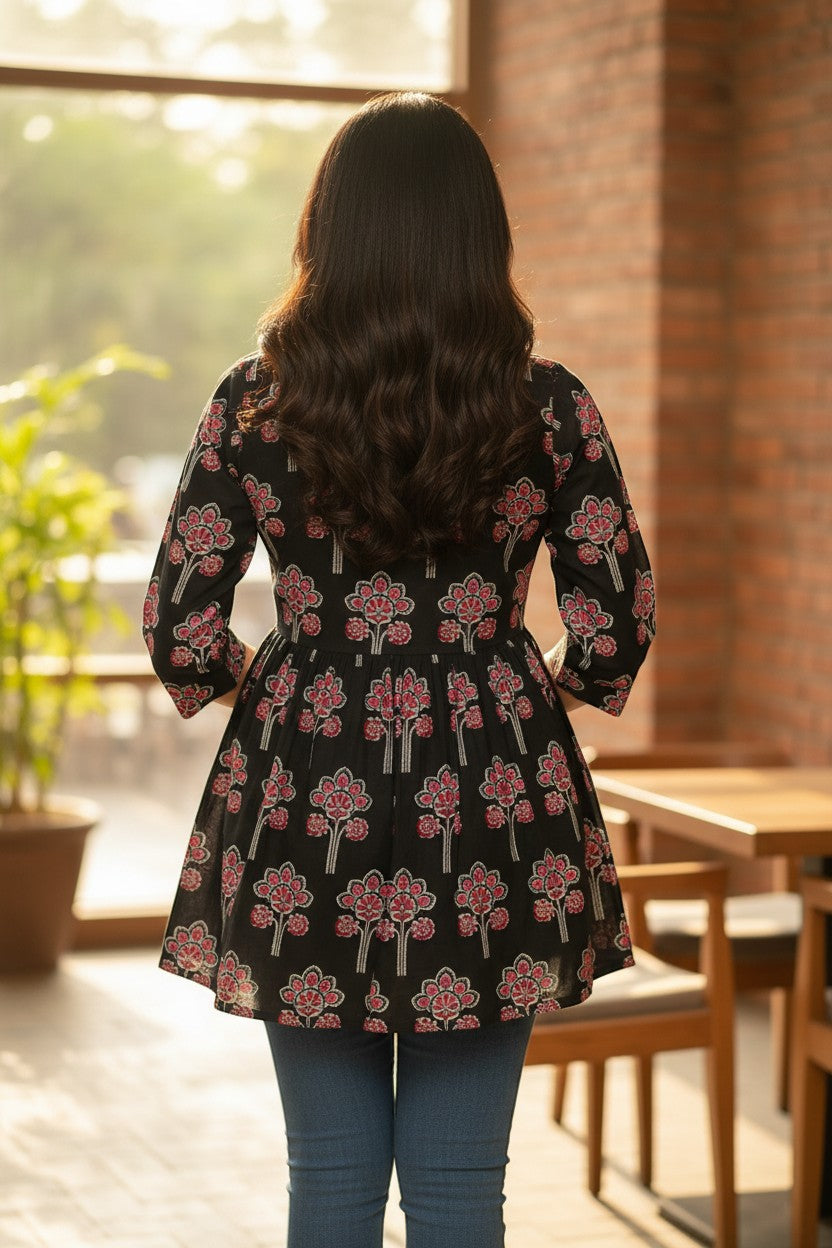 Naanu black cotton short kurti with pink and red lotus floral block print, gathered waist, and flared A-line silhouette.