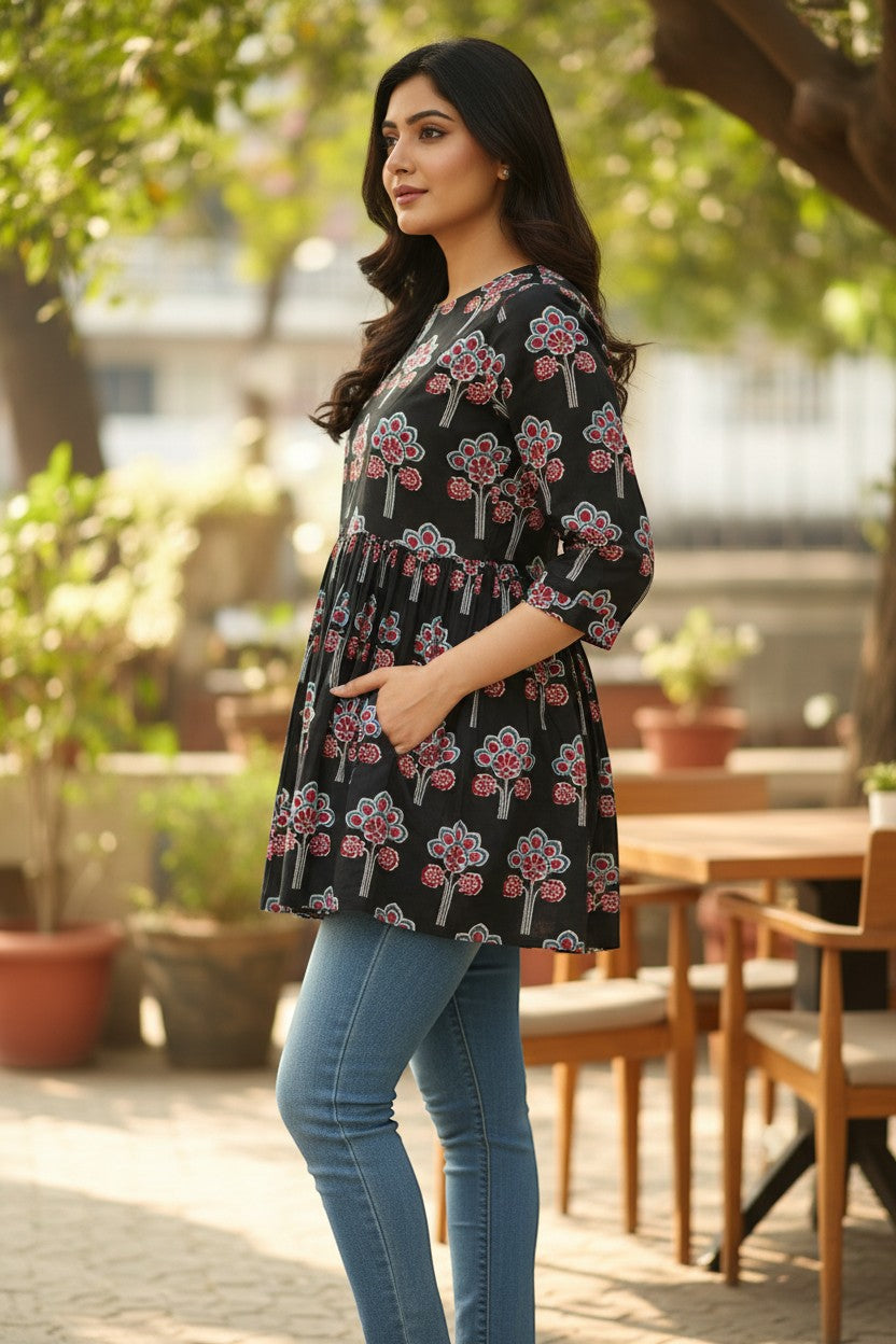 Naanu black cotton short kurti with pink, red, and white lotus floral block print, gathered waist, and 3/4 sleeves.