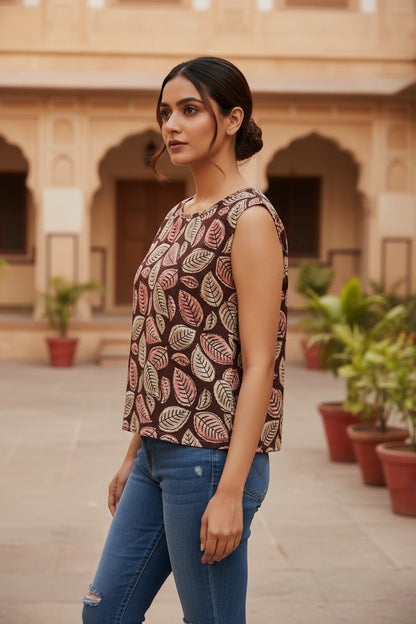 Naanu deep chocolate brown cotton top with scattered botanical leaf print in cream, blush pink, and dusty rose. Sleeveless with a wide round neckline.