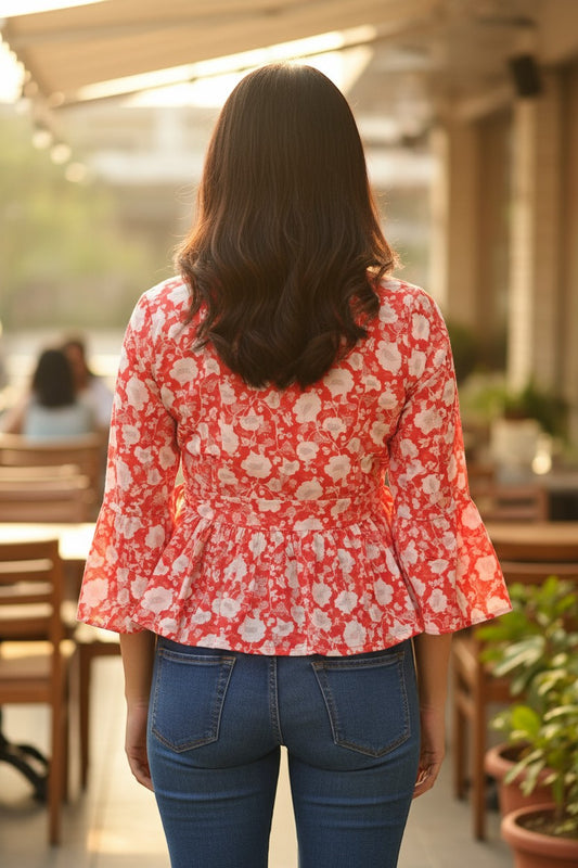 Naanu coral red cotton peplum top with white floral block print, bell sleeves, and tie waist, worn by a woman.