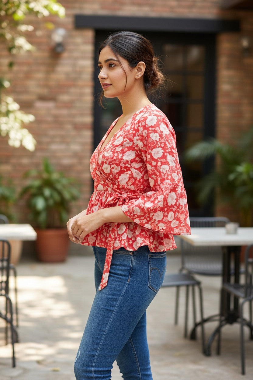 Naanu coral red cotton peplum top with white floral block print, V-wrap neckline, tie waist, and bell sleeves.