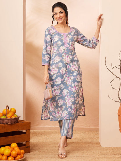 Naanu dusty blue floral print kurta with pink lace trim and 3/4 sleeves, paired with striped pants. Model wears the outfit with clear heels and a pink clutch.