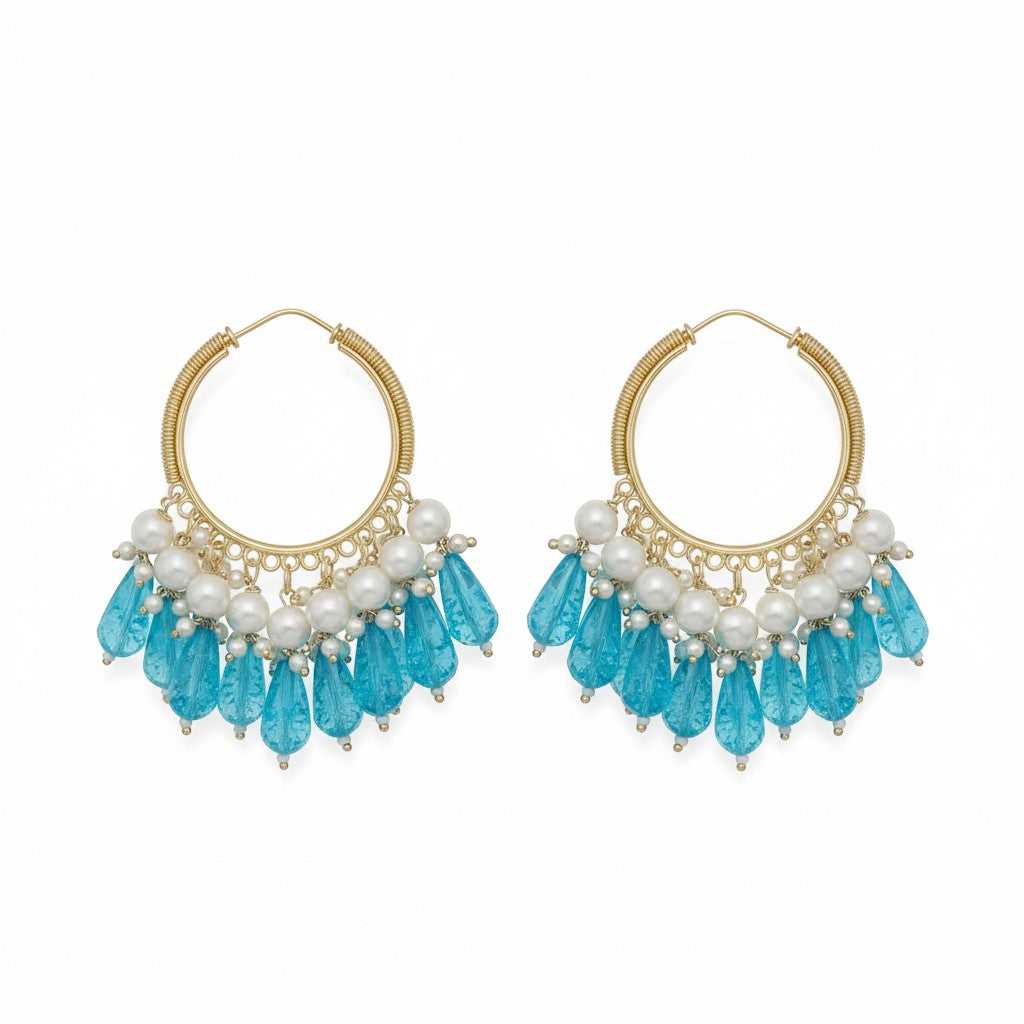 Naanu gold hoop earrings with pearl and blue crystal drops. Features gold wire-wrapped hoops with pearl clusters and faceted blue teardrop beads.