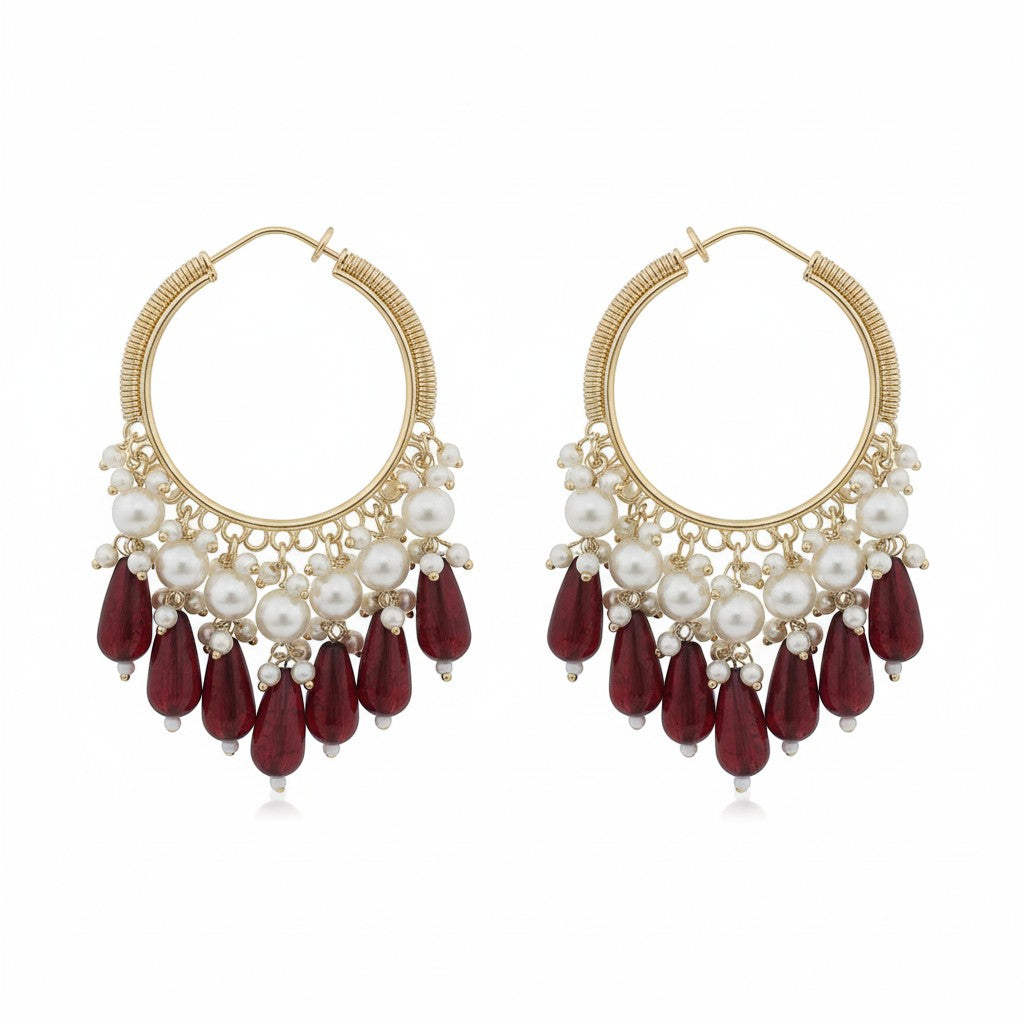 Naanu gold hoop earrings with pearl clusters and deep red crystal teardrop drops. Wire-wrapped coil hoop design.