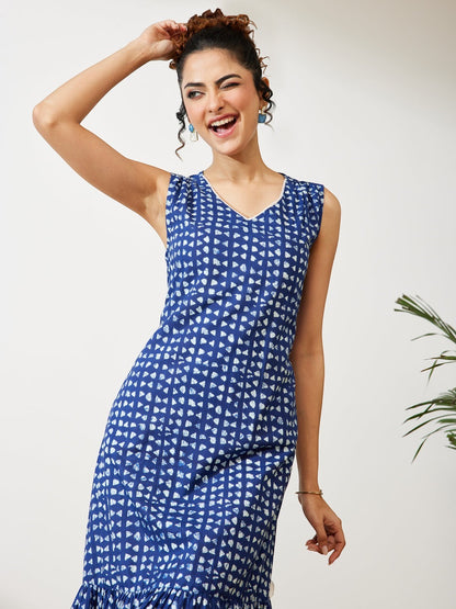 Naanu indigo blue sleeveless tiered midi dress with white geometric block print and V-neckline. Model winks and poses with hand on head.
