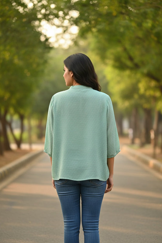 Naanu mint green georgette short shirt with 3/4 sleeves, mandarin collar, and pearl buttons. Model wears blue jeans.