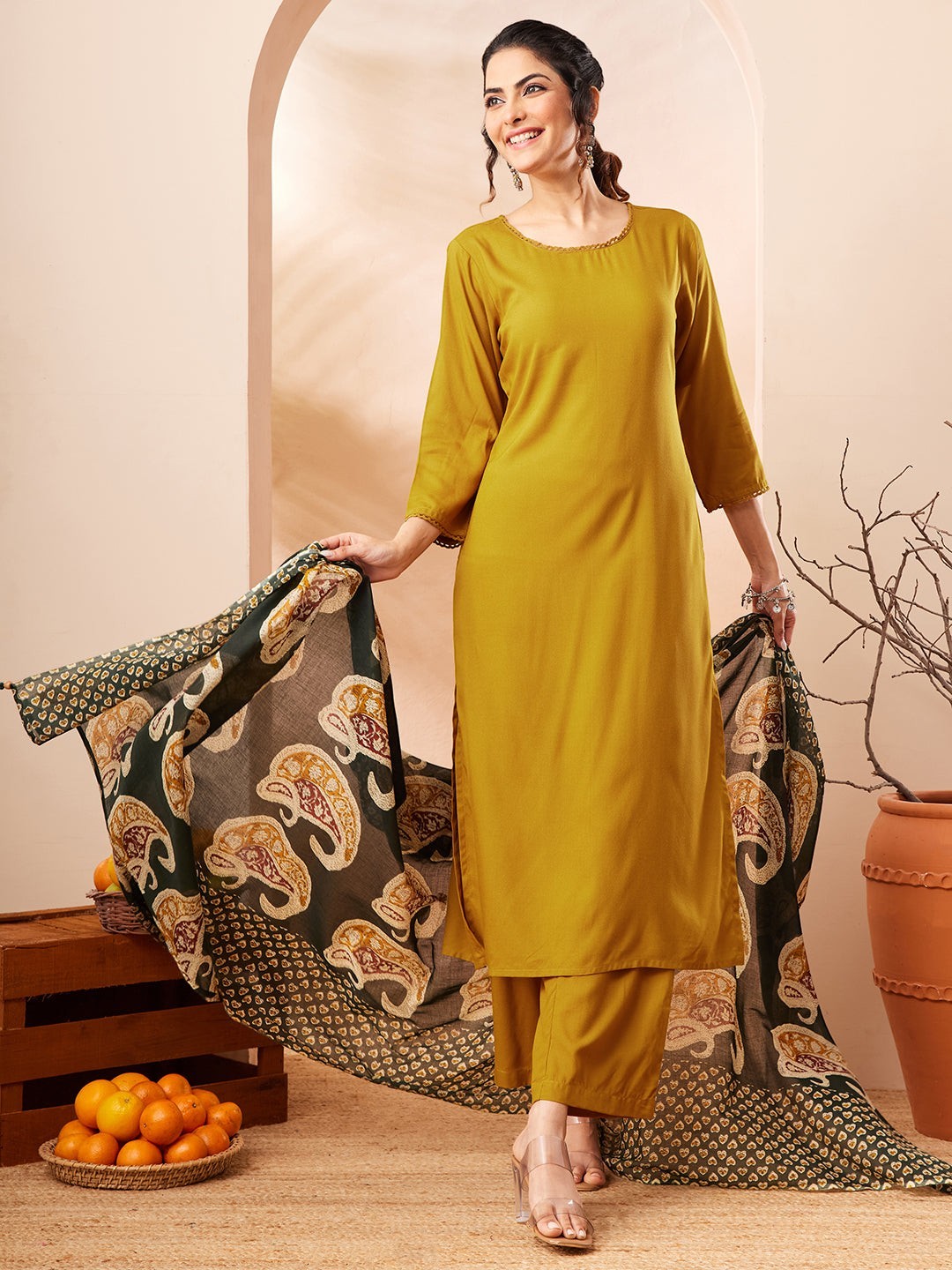 Naanu mustard yellow solid straight kurta with gold trim, palazzo pants, and a forest green paisley print dupatta.