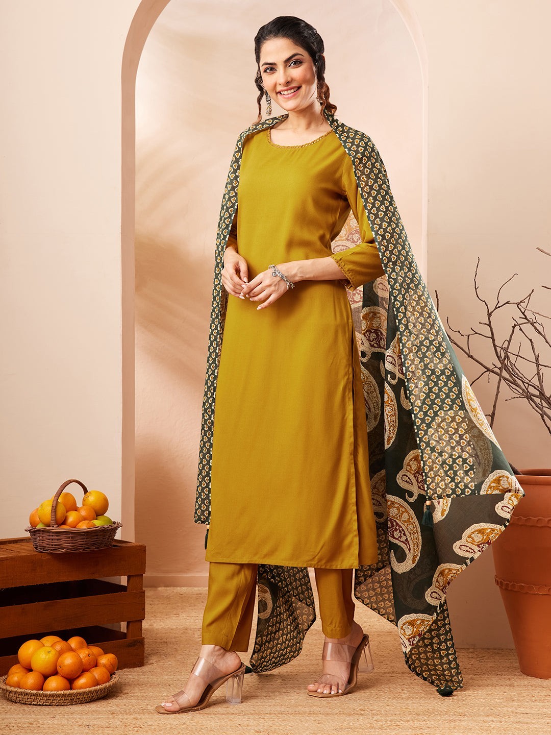Naanu mustard yellow solid straight kurta with gold trim, paired with matching palazzo pants and a forest green paisley dupatta.