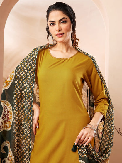 Naanu mustard yellow solid straight kurta with gold trim, palazzo pants, and a forest green paisley dupatta with tassel ends.