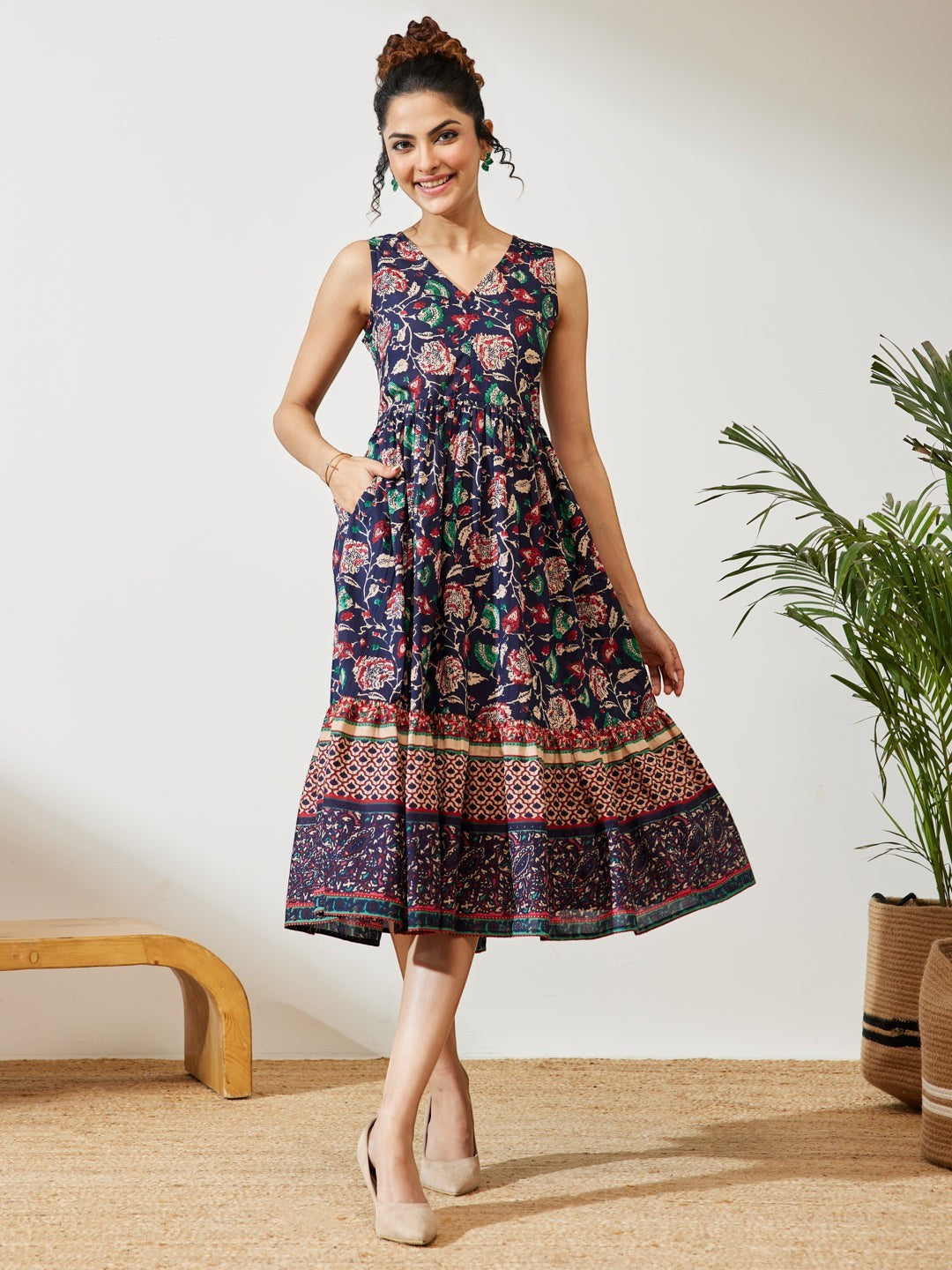 Naanu navy cotton midi dress with V-neck, empire waist, tiered border hem, and floral print. Sleeveless design with pockets.