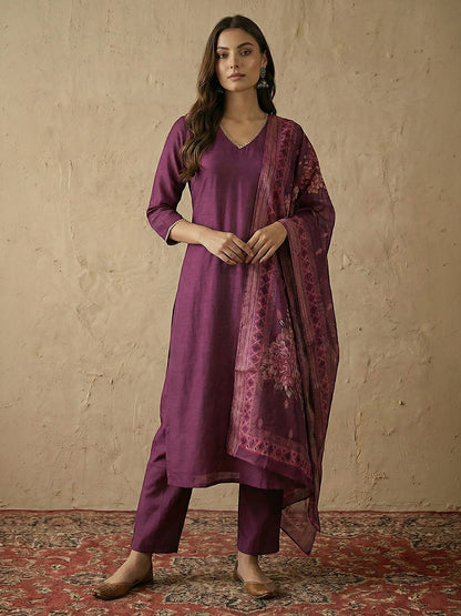 Naanu plum silk blend straight kurta set with V-neck, silver lace trim, and floral organza dupatta. Model is wearing matching pants and flats.