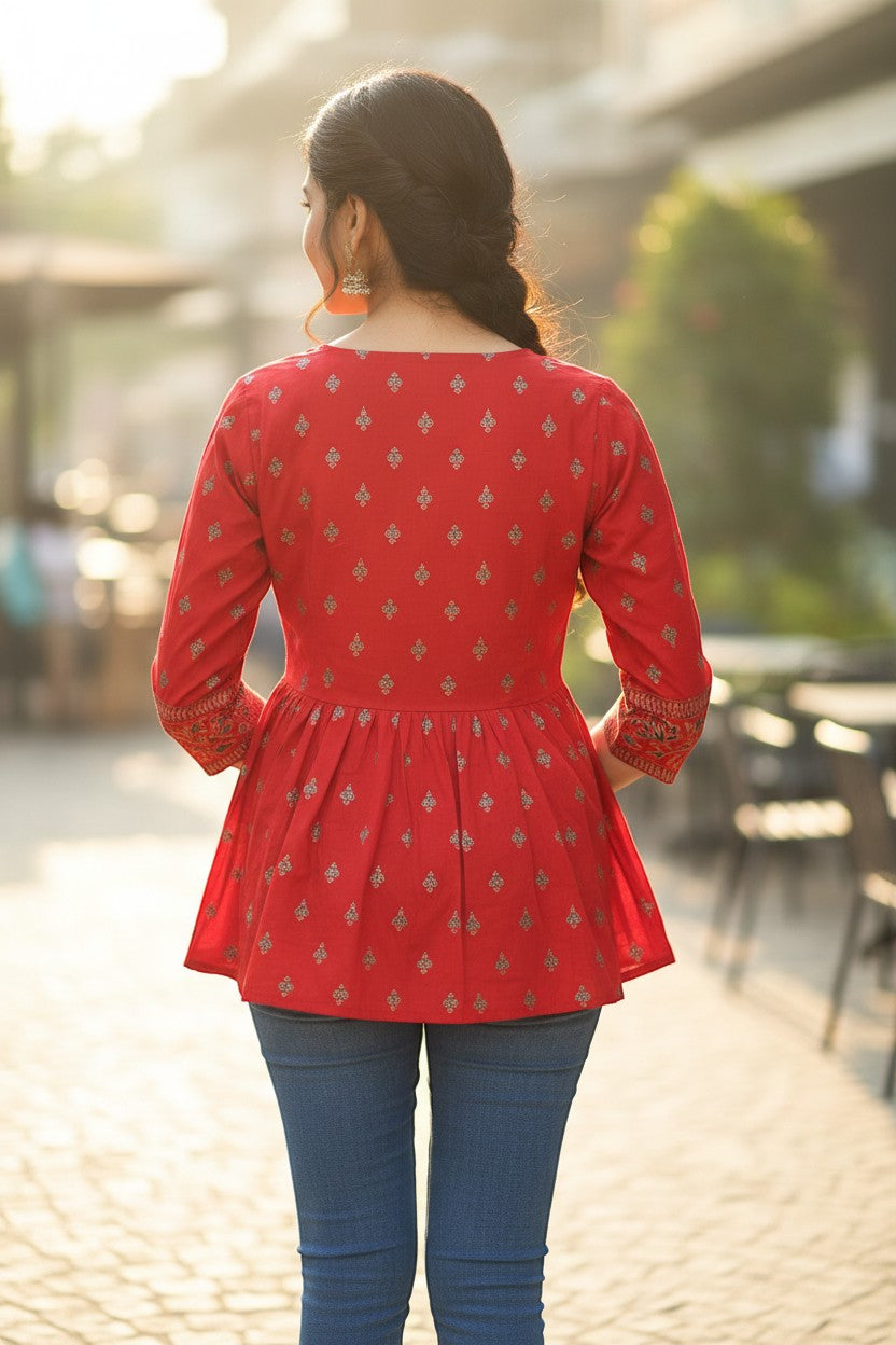 Naanu red rayon kurti with gold butti print, embroidered yoke, 3/4 sleeves, and peplum flare. Model wears blue jeans.