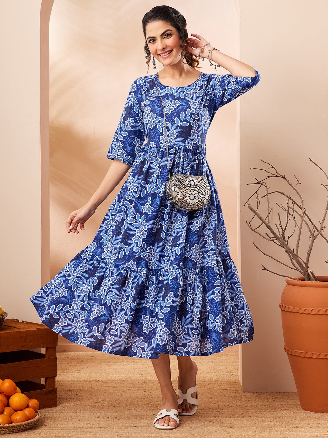 Naanu royal blue floral print tiered midi dress with 3/4 sleeves and round neckline. Model wears white sandals and a silver clutch.
