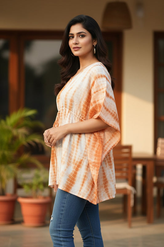 Naanu white and burnt orange shibori tie-dye cotton kaftan top with V-neck, tassel tie, batwing sleeves, and smocked waist.