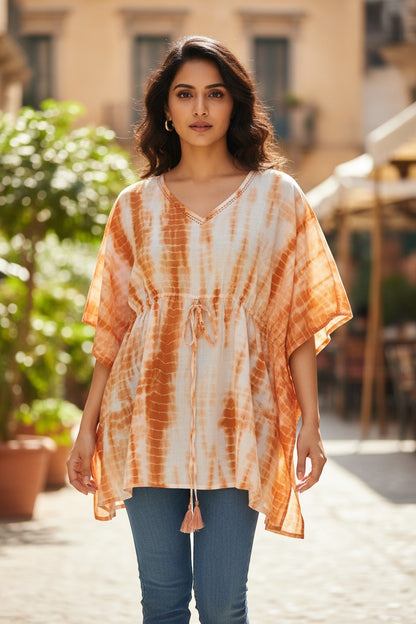 Naanu white and burnt orange shibori tie-dye cotton kaftan top with V-neck, tassel tie, batwing sleeves, and smocked waist.