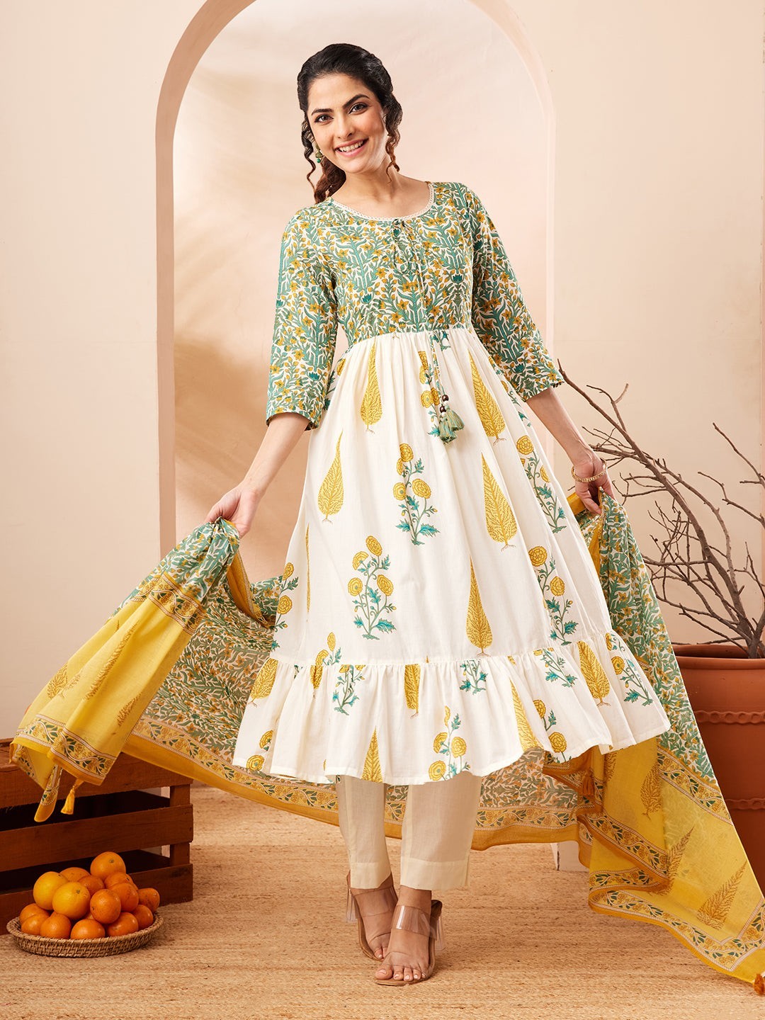 Naanu white cotton Anarkali kurta set with green floral block print, yellow dupatta with tassels. Model wears 3/4 sleeves and tiered hem.