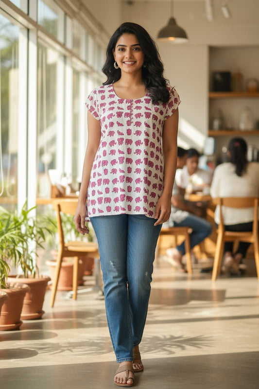 Naanu white cotton tunic with pink elephant print, scoop neck, short sleeves, and side slits, worn by a woman with jeans.